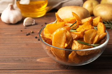 Glass bowl of delicious oven baked potatoes on table, closeup. Space for text