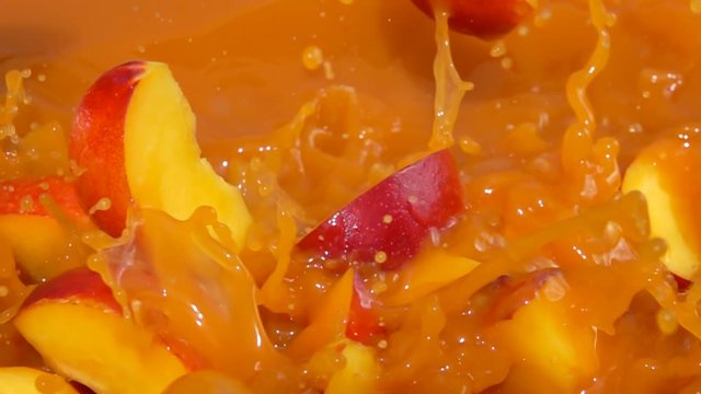 Slices of peach fall into juice with beautiful splashes in slow motion