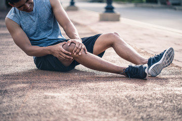 Fototapeta na wymiar Injury from workout concept : The man use hands hold on his knee while running on road in the park. Runner with injured knee in the park.