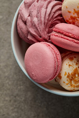 Gourmet sweet pink macaroons with soft pink zephyr in white and blue bowl on gray background