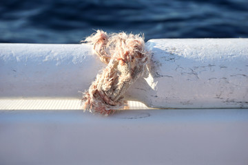 Broken rope tied in a knot around part of the old wooden paddle on the white boat with sea surface in the background