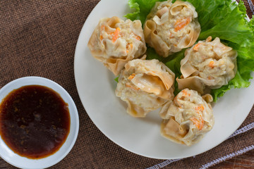 Chinese Steamed Dumpling (Shumai) on white dish served with soy sauce and .lettuce leaves on brown cloth and wooden table. Delicious Dimsum pork.