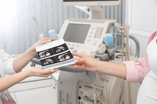 Doctor showing ultrasound images of baby to future mother in clinic, closeup