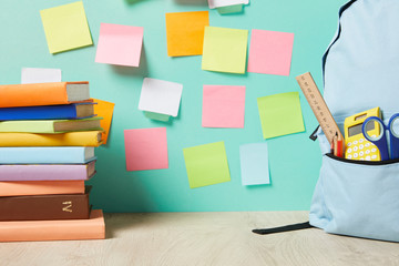 blue backpack with supplies in pocket near books and multicolored sticky notes on turquoise wall