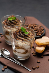Classic tiramisu dessert in a glass cup on brown kitchen towel or napkin on dark concrete background