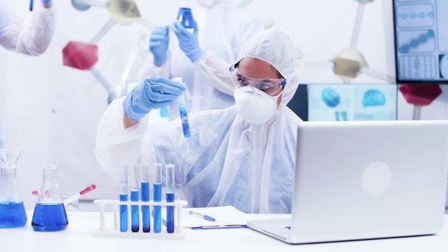 Female scientis holding a test tube with smoking blue fluid and writing formula. Chemistry lab with smoking fluid making bubles.