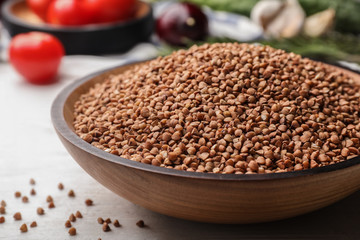 Wooden bowl of buckwheat on white table, closeup