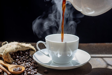 The steam from Pouring coffee into cup , A cup of fresh coffee on rusty metal wall with copy space. A scattering of coffee beans with a cup of coffee. Coarse fabric ,hot food and healthy meal concept