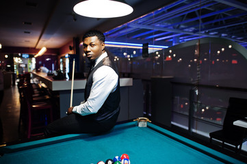 Young handsome african man wearing white shirt, black vest and bow tie play pool billiard.