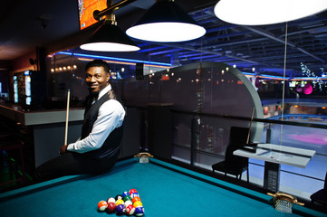 Young handsome african man wearing white shirt, black vest and bow tie play pool billiard.