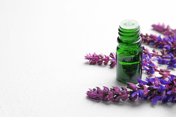 Bottle of sage essential oil and flowers on light table, space for text