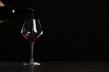 Woman pouring wine into glass on table against black background, closeup with space for text