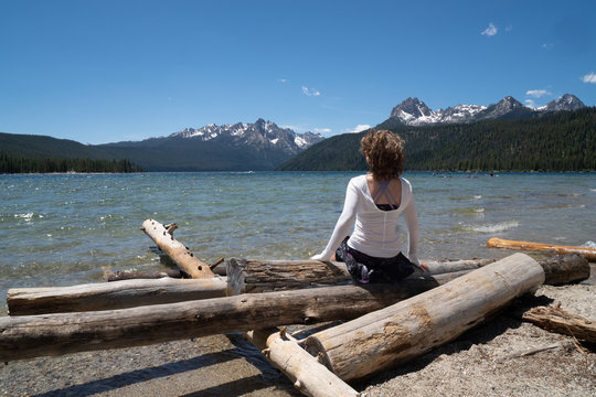 Adult woman (30-35 years) sits on a pile of logs on the shoreline of Redfish Lake in Stanley Idaho in the Sawtooth Mountains in summer