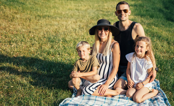 Picture of young parents with son and daughter sitting on plaid on picnic on summer day