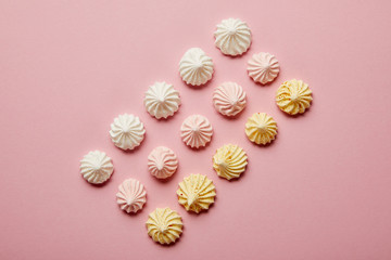 Top view of white, pink and yellow meringues in rows on pink background