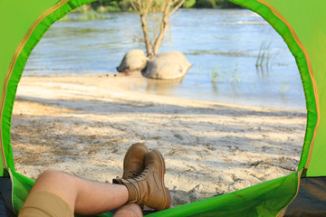 Young man resting in camping tent on riverbank, view from inside