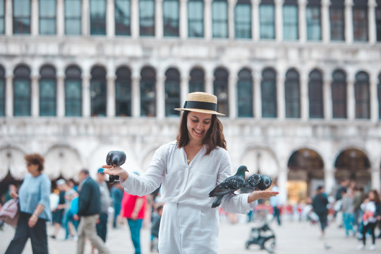 woman in white clothes with straw hat having fun with pigeons at venice city square
