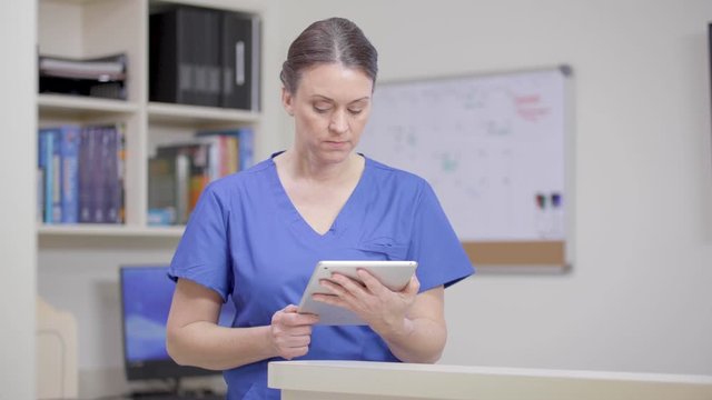 Nurse at station reviews the patient record on tablet, camera moves right.