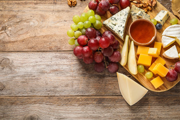 Flat lay composition with board of delicious cheese and snacks on wooden background. Space for text