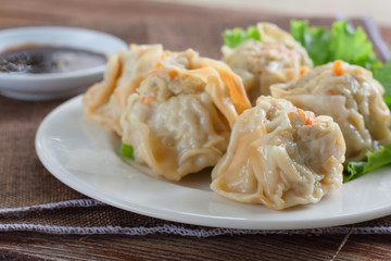 Chinese Steamed Dumpling (Shumai) on white dish served with soy sauce and .lettuce leaves on brown cloth and wooden table. Delicious Dimsum pork.