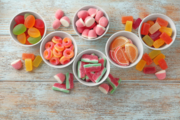 Flat lay composition with bowls of different jelly candies on wooden background