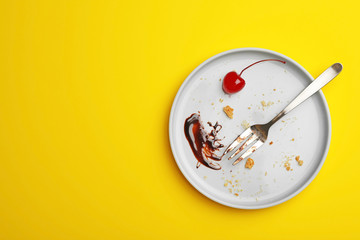 Dirty plate with food leftovers, fork and canned cherry on yellow background, top view. Space for text
