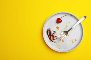 Dirty plate with food leftovers, fork and canned cherry on yellow background, top view. Space for...