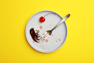 Dirty plate with food leftovers, fork and canned cherry on yellow background, top view