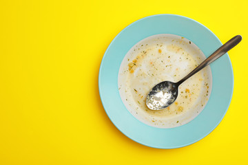 Dirty plate with food leftovers and spoon on yellow background, top view. Space for text