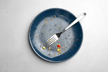 Dirty plate with food leftovers and fork on grey background, top view