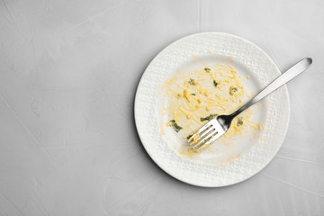 Dirty plate with food leftovers and fork on grey background, top view. Space for text