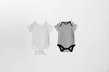 Different baby onesies hanging on clothes line against light grey background. Laundry day