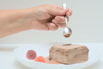 On a white plate is coffee ice cream and two marmalades. In a female hand a teaspoon. A woman is trying ice cream. Concert - dessert