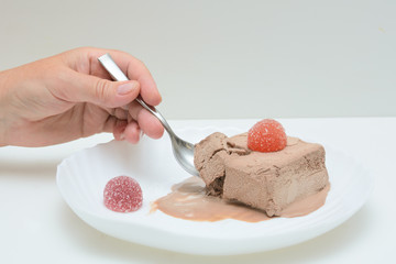 On a white plate is coffee ice cream and two marmalades. In a female hand a teaspoon. A woman is trying ice cream. Concert - dessert