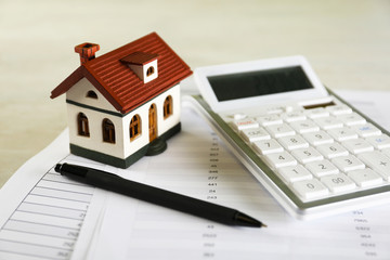 Calculator, house model, pen and documents on light table. Real estate agent's workplace