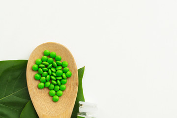 Alternative medicine and homeopathic tablets. Wooden spoon with green pills and glass bottle on a white background. Homeopathy medicine concept. Top view. Copy space