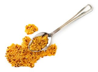 Mustard grains spilled from a metal spoon on a white. The view of the top.