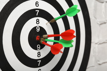 Arrows hitting dart board on white textured wall, closeup