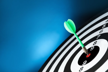 Green arrow hitting target on dart board against blue background. Space for text