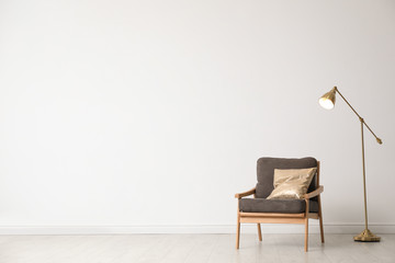 Stylish living room interior with wooden armchair and floor lamp near white wall. Space for text