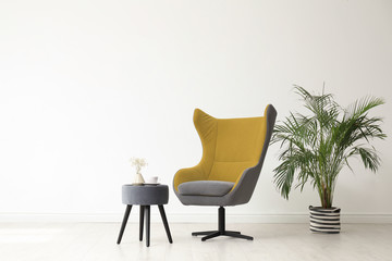 Fototapeta premium Stylish living room interior with comfortable armchair and houseplant near white wall. Space for text