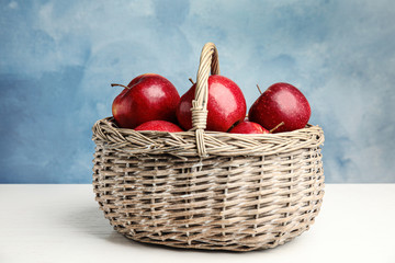 Wicker basket with ripe juicy red apples on white wooden table against blue background