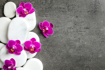 White spa stones and orchid flowers on grey background, flat lay. Space for text