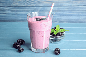Fototapeta na wymiar Delicious blackberry smoothie in glass on blue wooden table