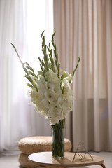 Vase with beautiful white gladiolus flowers on wooden table in room, space for text