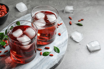 Healthy goji juice with ice in glasses on grey table. Space or text