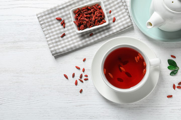 Healthy goji tea in cup served on white wooden table, flat lay. Space for text