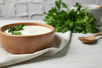 Bowl of fresh sour cream with parsley and wooden spoon on white wooden table. Space for text