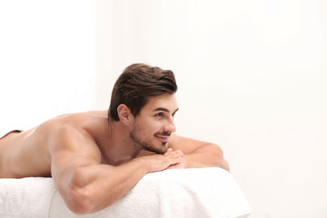 Fototapeta na wymiar Handsome young man relaxing on massage table against light background, space for text. Spa salon
