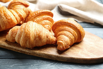 Board with tasty croissants on dark wooden table, closeup. French pastry